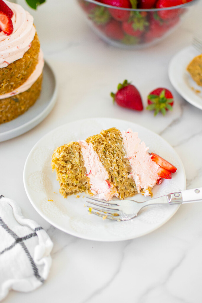 slice of eggless strawberry zucchini cake on a plate with a fork on a white marble table.