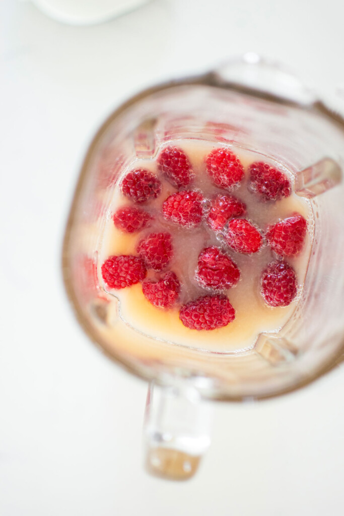 fresh raspberries and lemon juice in a glass blender on a white marble countertop.