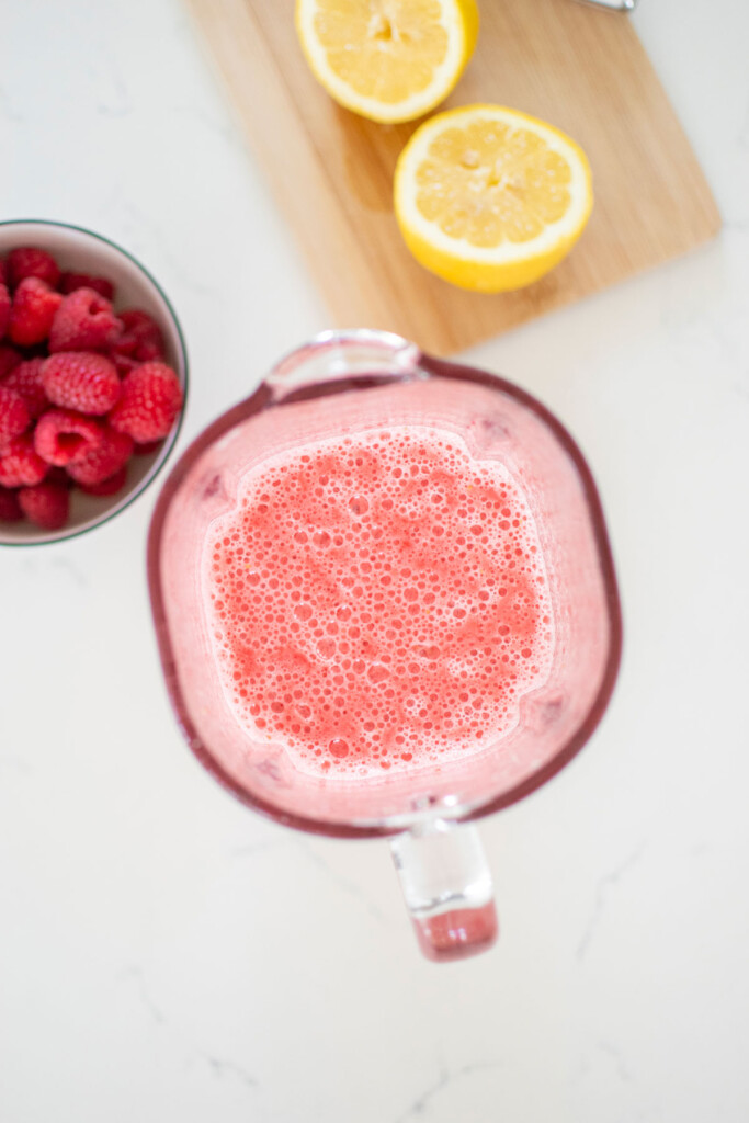 blended raspberries and lemon juice in a glass blender on a white marble countertop.