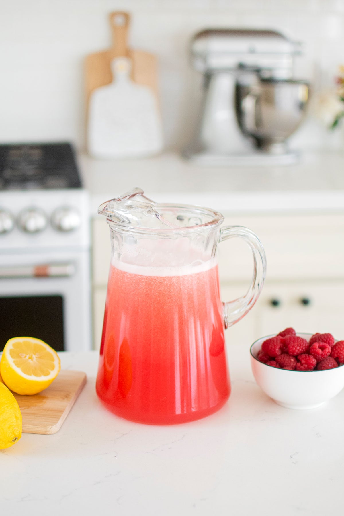 glass pitcher of organic pink lemonade on the kitchen counter with fresh raspberries and lemons.