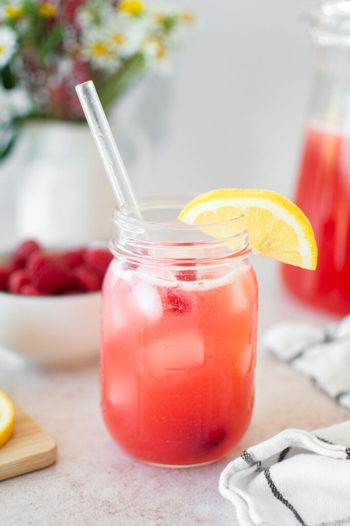 organic pink lemonade in a mason jar with a glass straw and fresh lemon slice.
