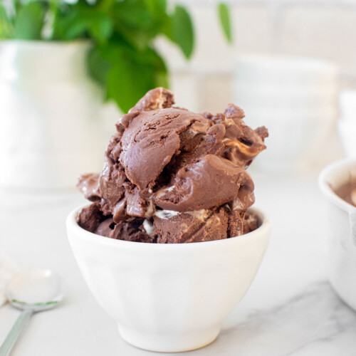 two scoops of organic rocky road ice cream in a small bowl on a white marble countertop.