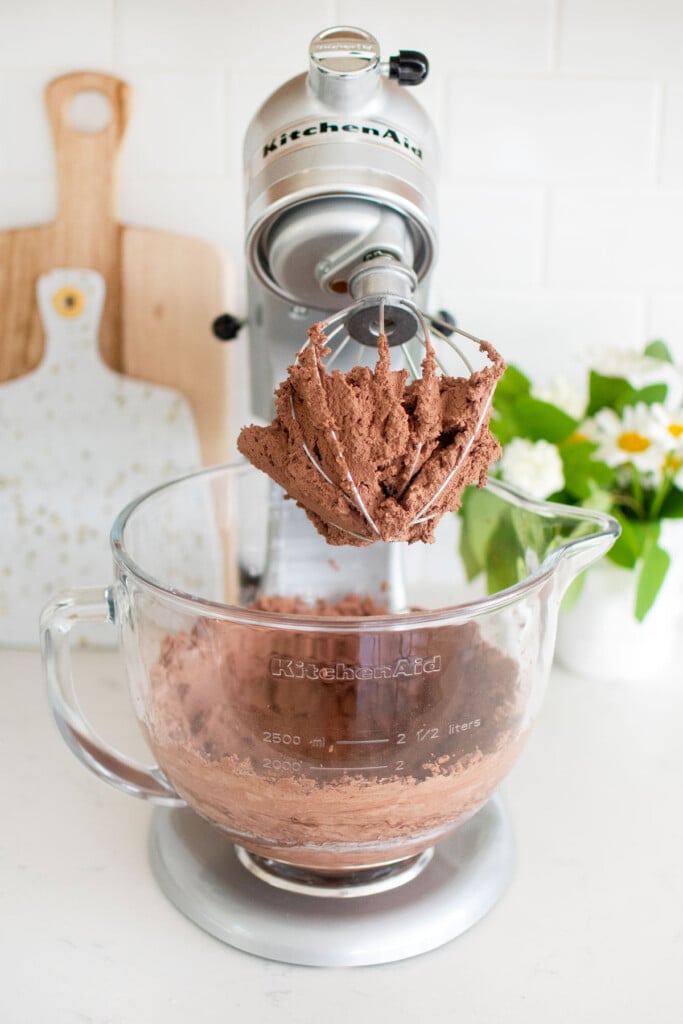 chocolate whipped cream on a whisk in a stand mixer on a white marble countertop.