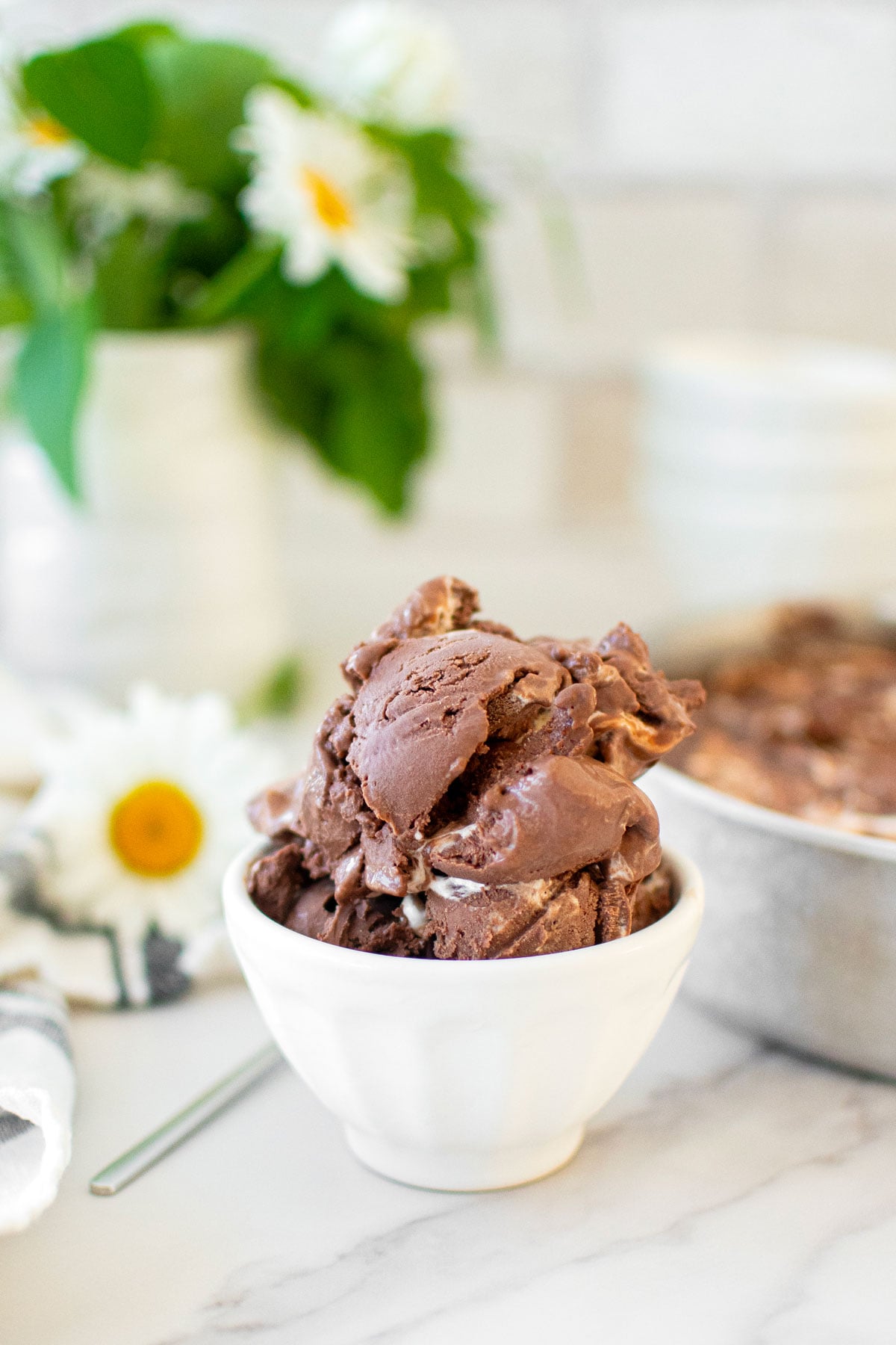 two scoops of organic rocky road ice cream in a small bowl on a white marble countertop.
