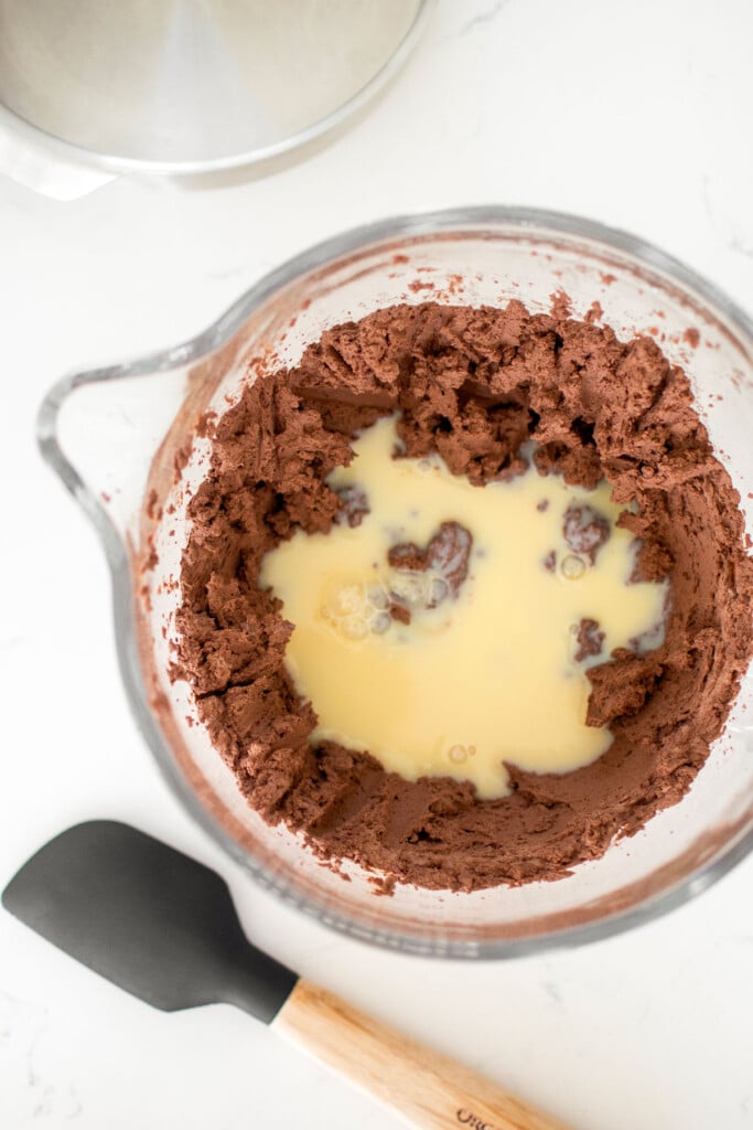 chocolate whipped cream and sweetened condense milk in a glass mixing bowl on a white countertop.