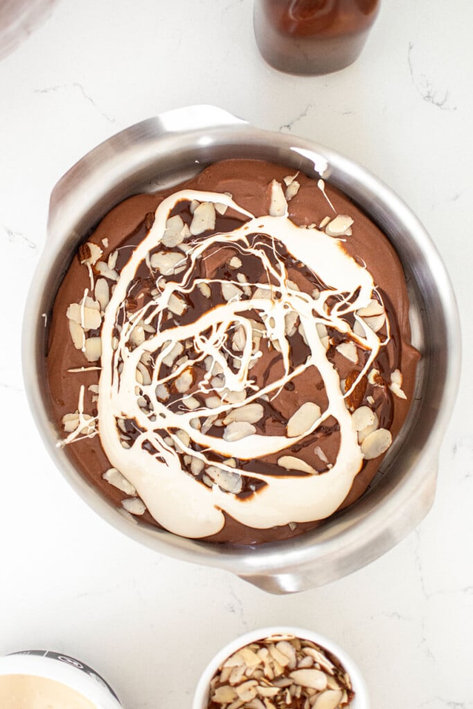 organic rocky road ice cream being swirled with marshmallow creme in a pan on a white marble countertop.