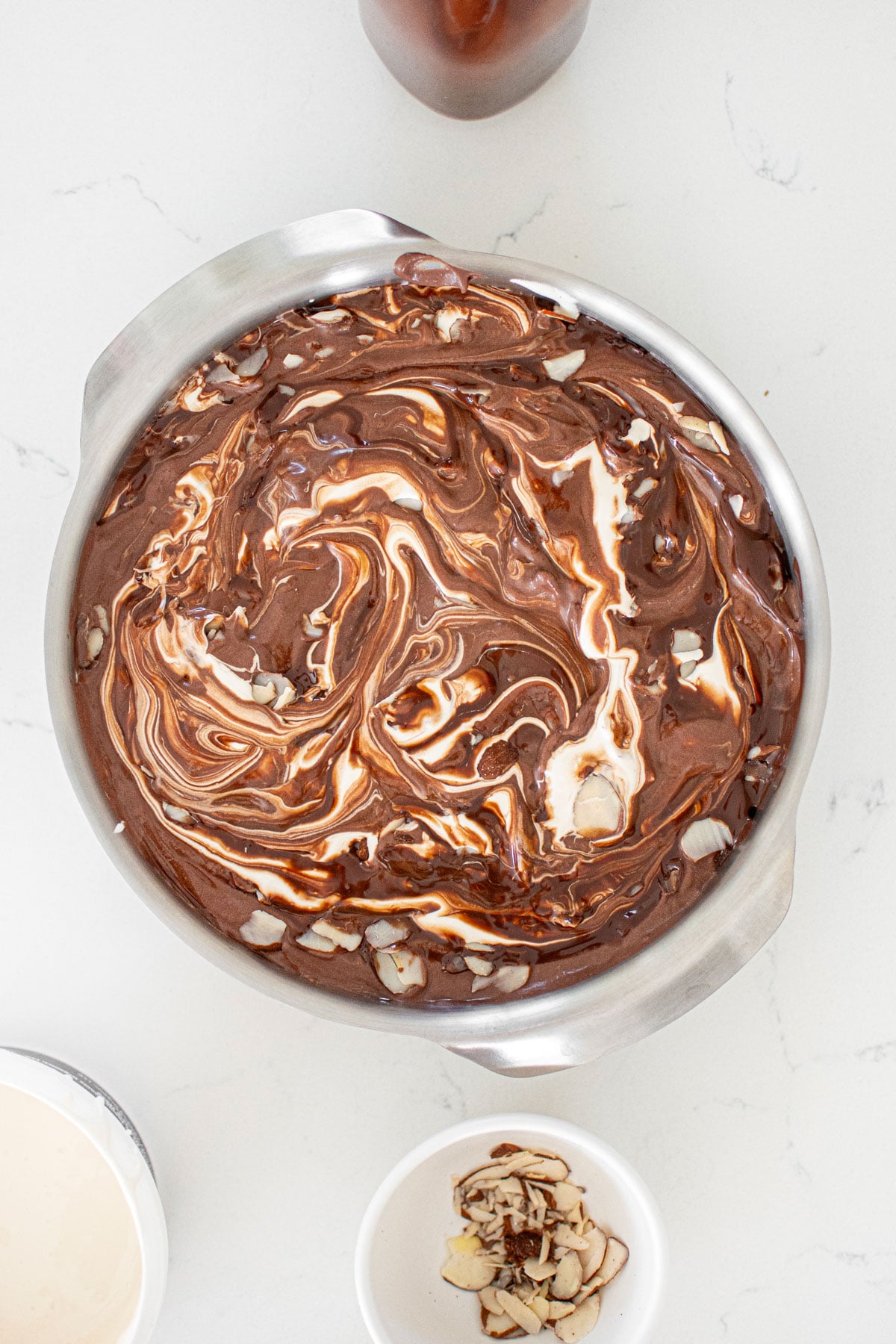 organic rocky road ice cream being swirled with marshmallow creme in a pan on a white marble countertop.