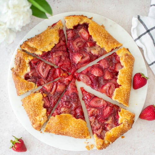 eggless strawberry honey galette on a marble serving board cut into slices on a table with fresh flowers.