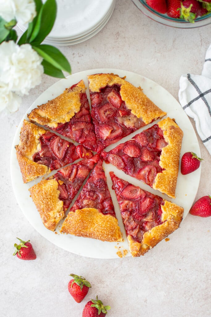 eggless strawberry honey galette on a marble serving board cut into slices on a table with fresh flowers.