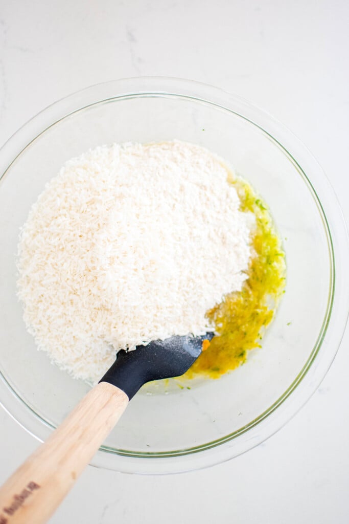 zucchini dog cake batter getting mixed together in a glass mixing bowl on a white marble countertop.