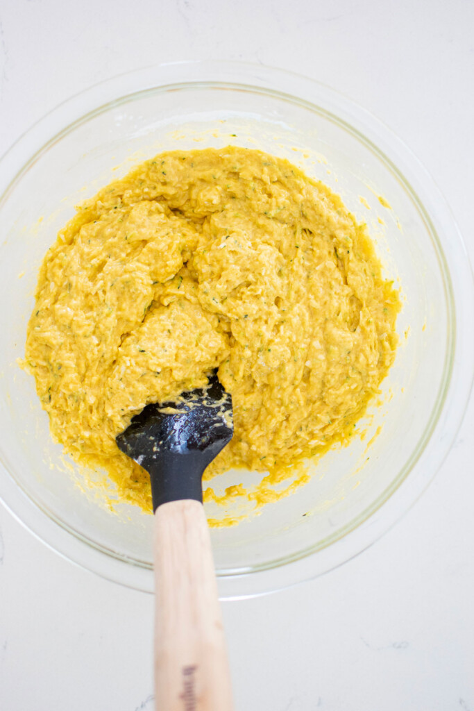 zucchini dog cake batter getting mixed together in a glass mixing bowl on a white marble countertop.