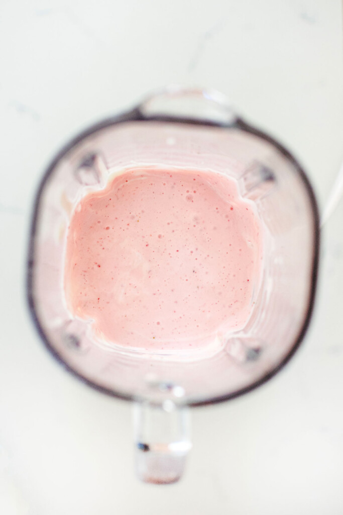 strawberries and greek yogurt blended together in a glass blender on a white marble countertop.