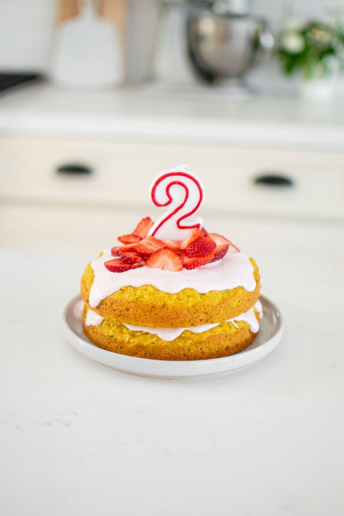 strawberry zucchini cake for dogs with a number 2 candle on top on a marble countertop.