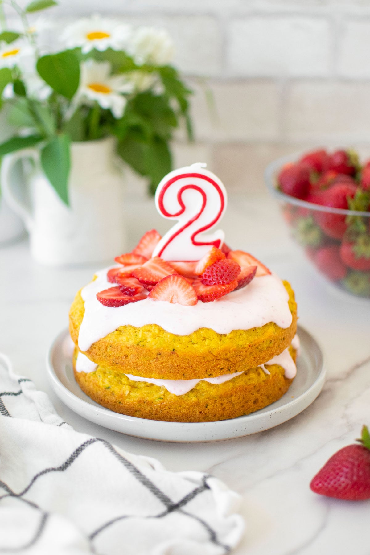 strawberry zucchini cake for dogs with a number 2 candle on top on a marble countertop.