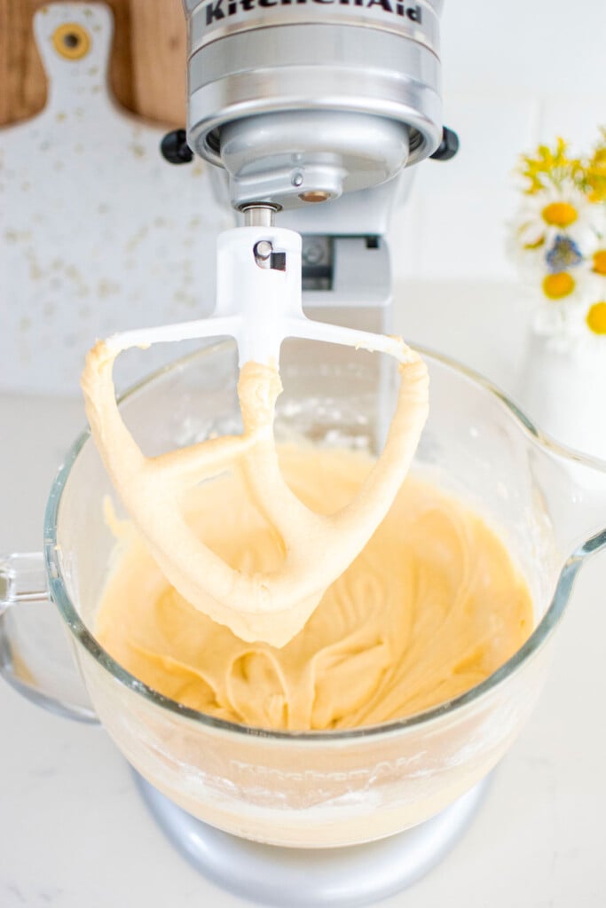 birthday bundt cake batter in a glass stand mixing bowl on a marble counter with a vase of flowers.