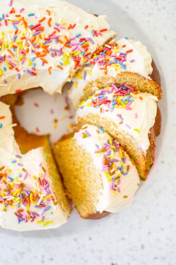 birthday bundt cake with rainbow sprinkles cut into slices on a marble cake plate.