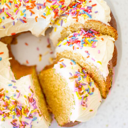 birthday bundt cake with rainbow sprinkles cut into slices on a marble cake plate.