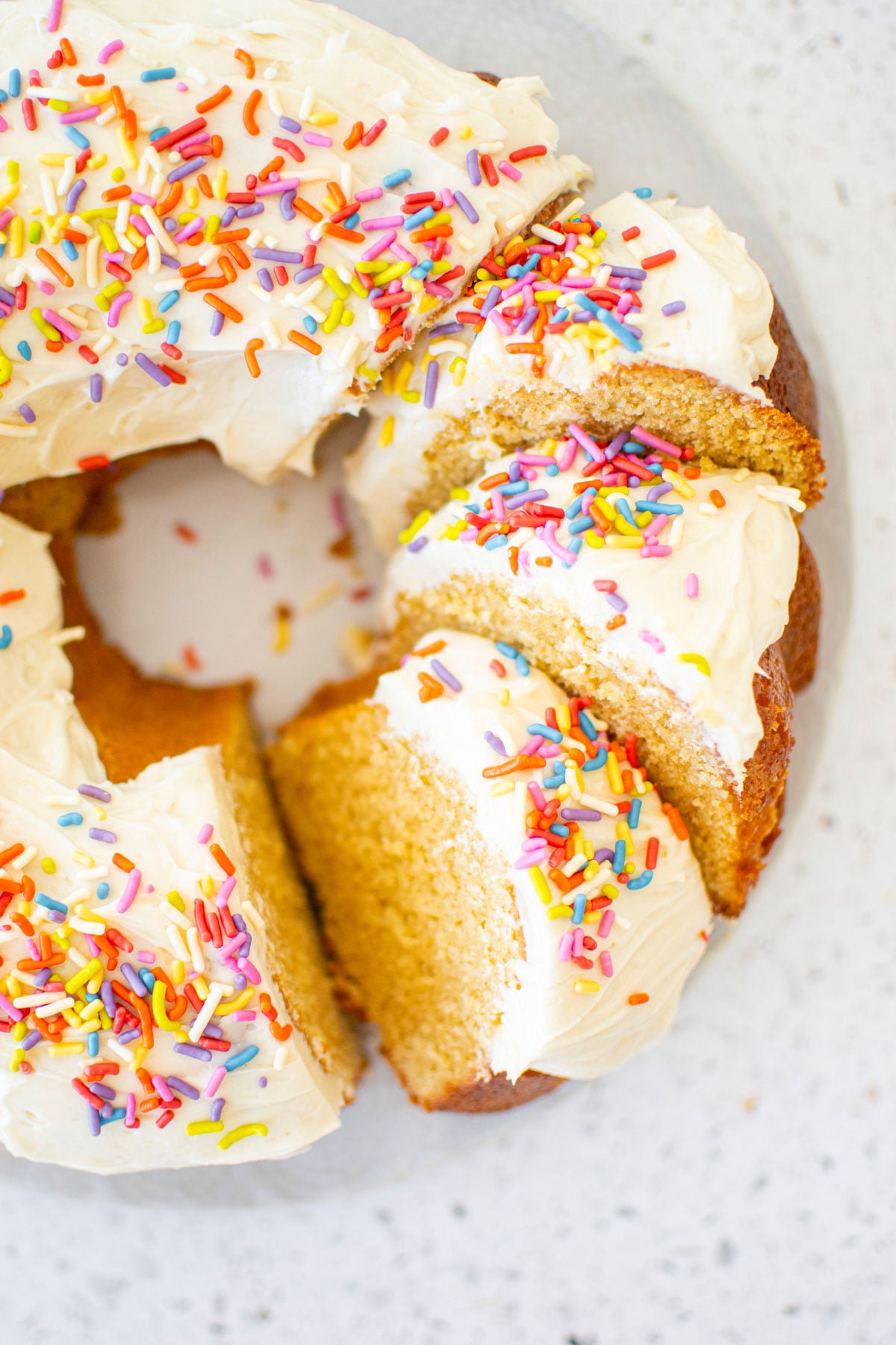 birthday bundt cake with rainbow sprinkles cut into slices on a marble cake plate.
