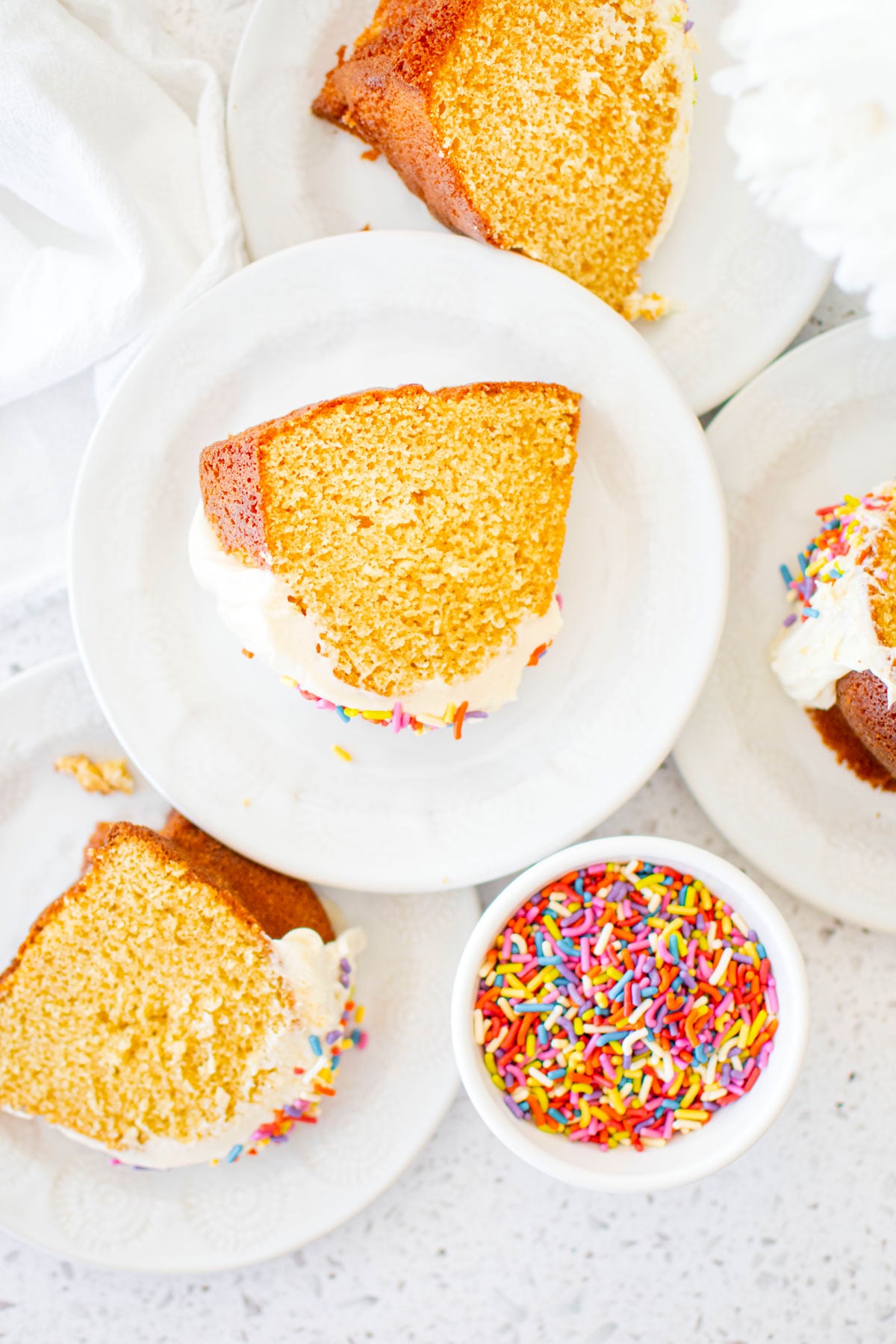 slices of birthday bundt cake on a white cake plates on a white marble counter with a bowl of sprinkles.