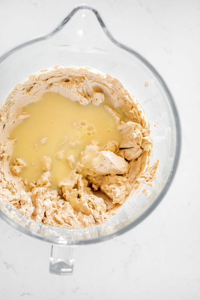 no churn coffee ice cream being mixed in a glass mixing bowl on a white marble counter.