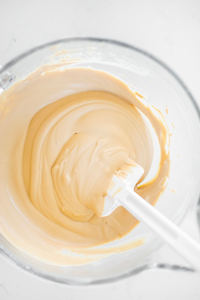 no churn coffee ice cream being mixed in a glass mixing bowl on a white marble counter.