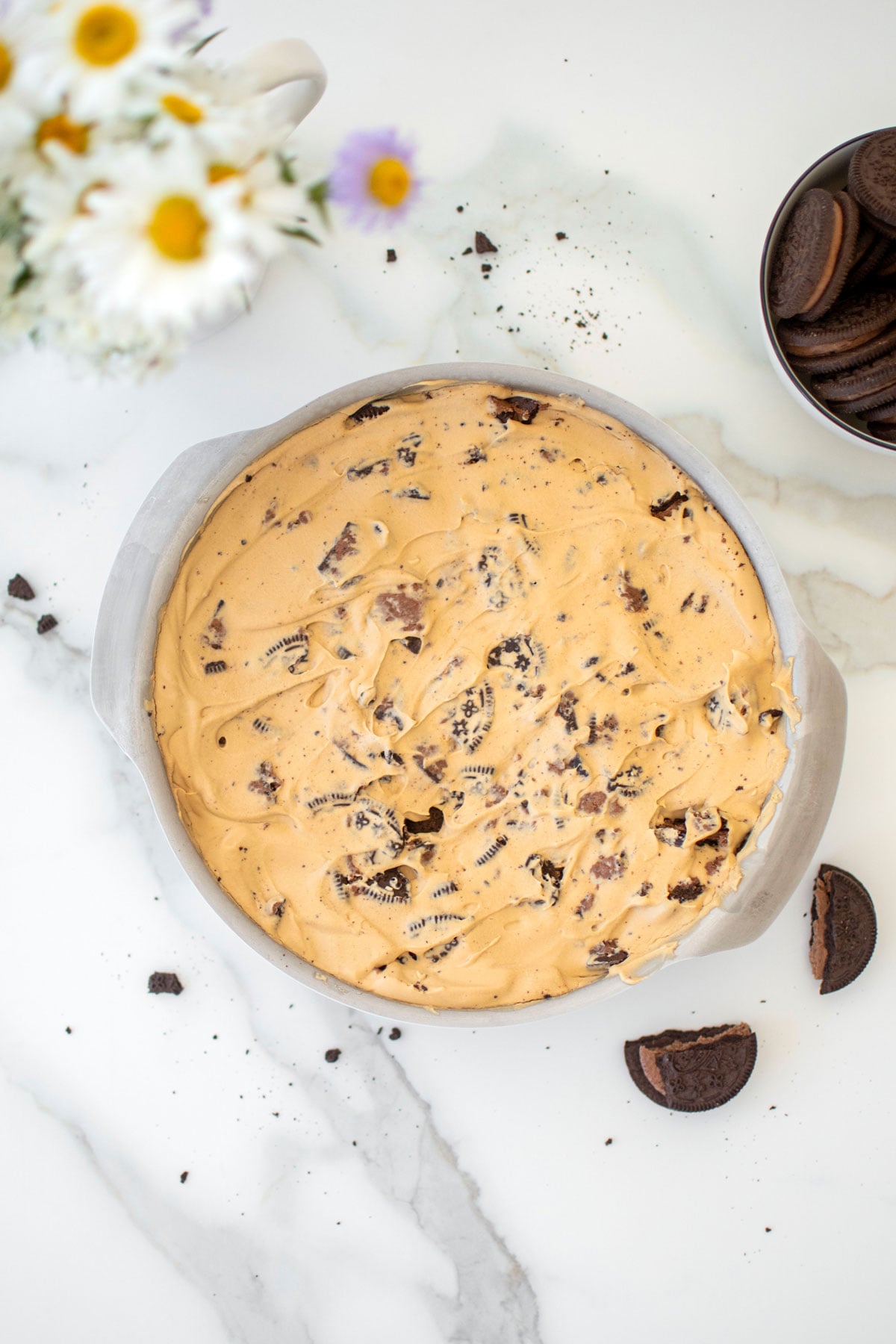 cookies and cream coffee ice cream in a cake pan on a white marble counter.