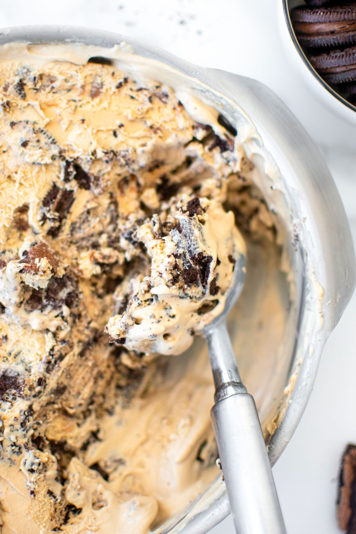 cookies and cream coffee ice cream in a cake pan on a white marble counter being scooped with an ice cream scoop.