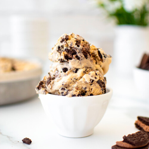 two scoops of cookies and cream coffee ice cream in a small dish on a white marble counter with fresh flowers.