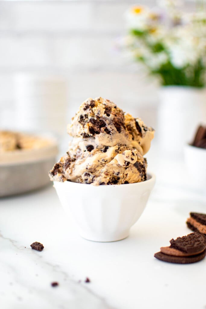 two scoops of cookies and cream coffee ice cream in a small dish on a white marble counter with fresh flowers.