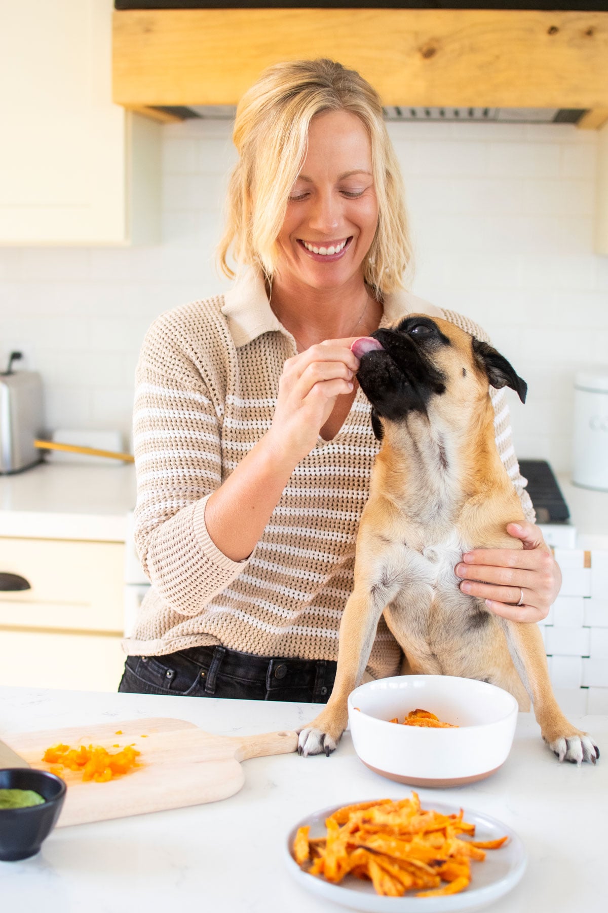 woman and pug in kitchen feeding pug homemade beef dog food at the kitchen counter.