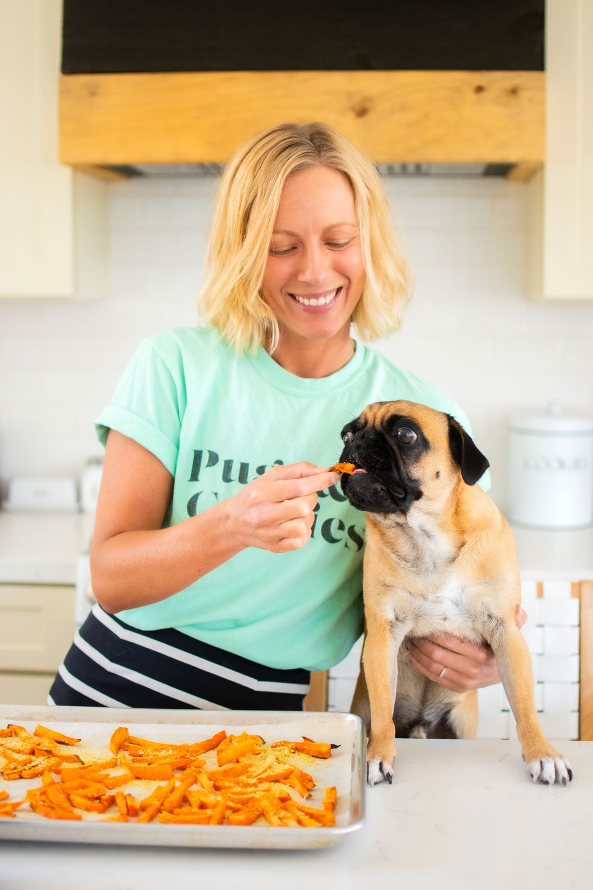 woman and pug in kitchen eating dog friendly sweet potato fries at kitchen counter.
