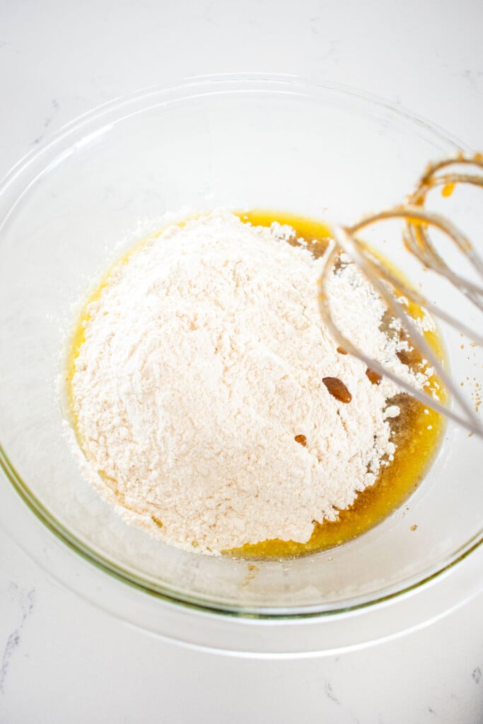 dry ingredients for olive oil strawberry blondies being mixed in a glass mixing bowl on a white marble counter.