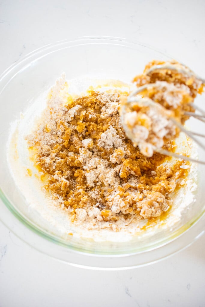 olive oil strawberry blondies being mixed in a glass mixing bowl on a white marble counter.
