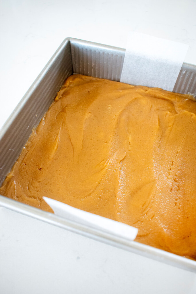 olive oil strawberry blondies spread into a square baking pan on a white marble counter.