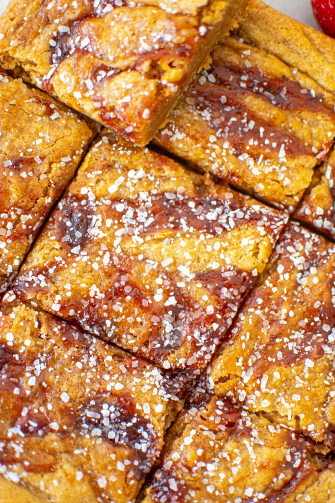 olive oil strawberry blondies cut into squares on a wood cutting board with white parchment paper.