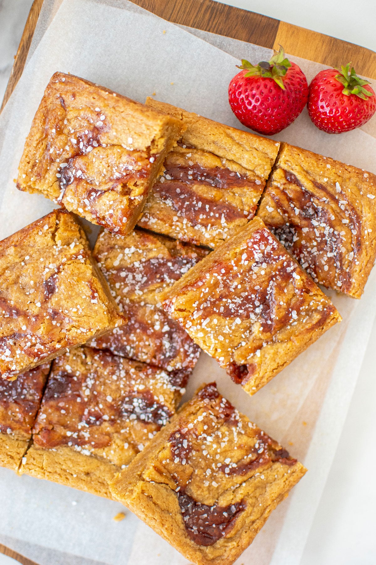 olive oil strawberry blondies cut into squares on a wood cutting board with white parchment paper.