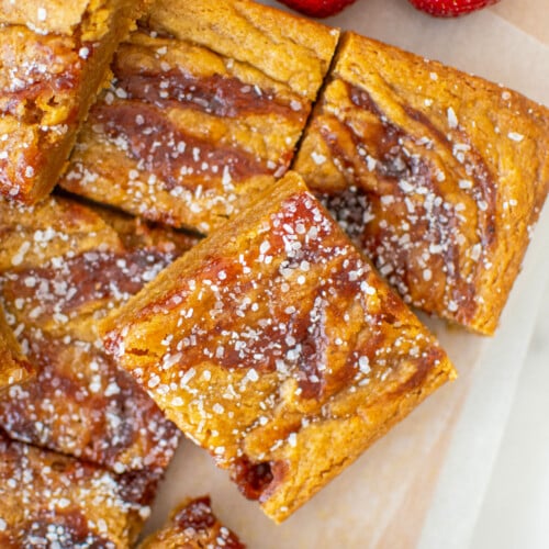 olive oil strawberry blondies cut into squares on a wood cutting board with white parchment paper.