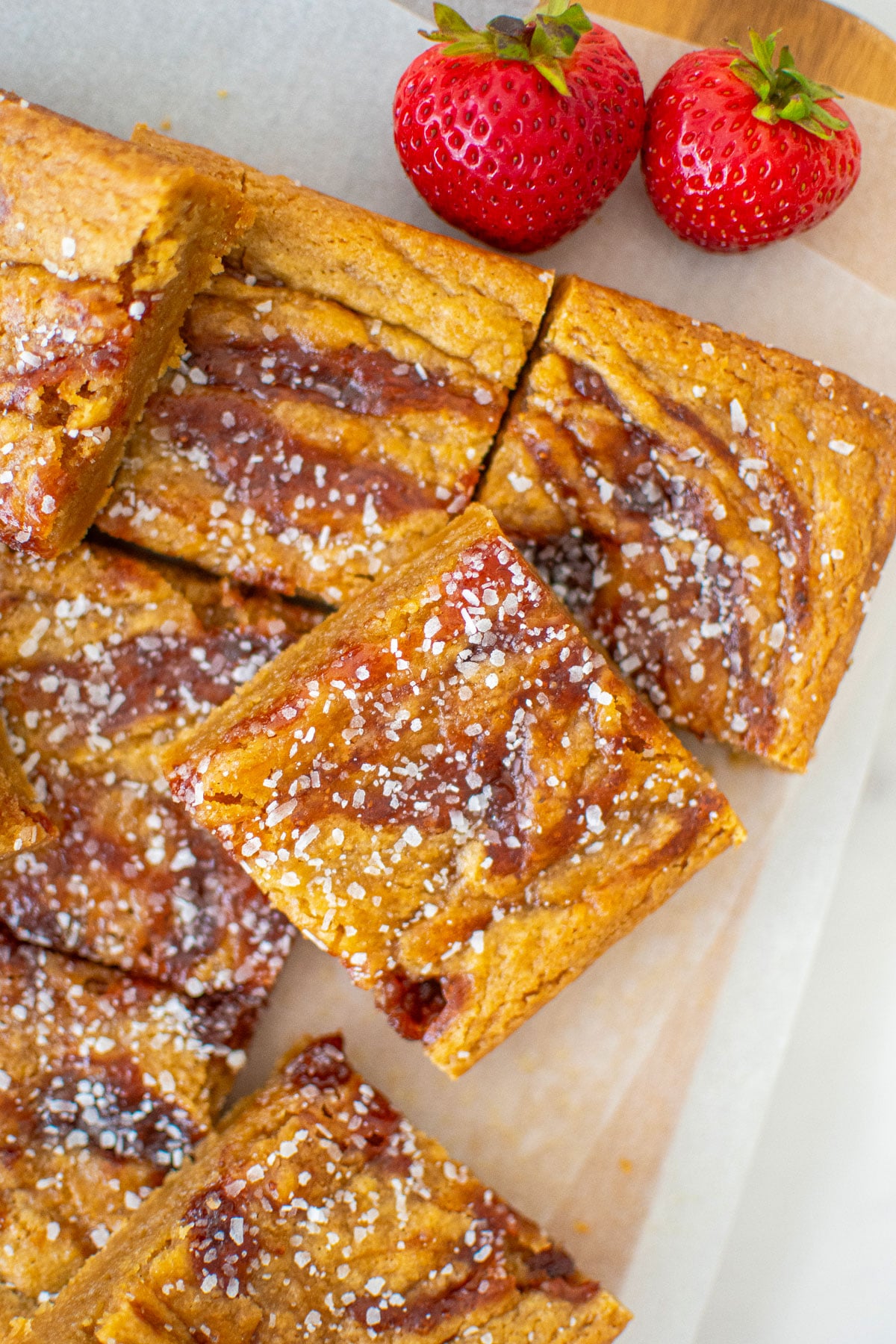 olive oil strawberry blondies cut into squares on a wood cutting board with white parchment paper.