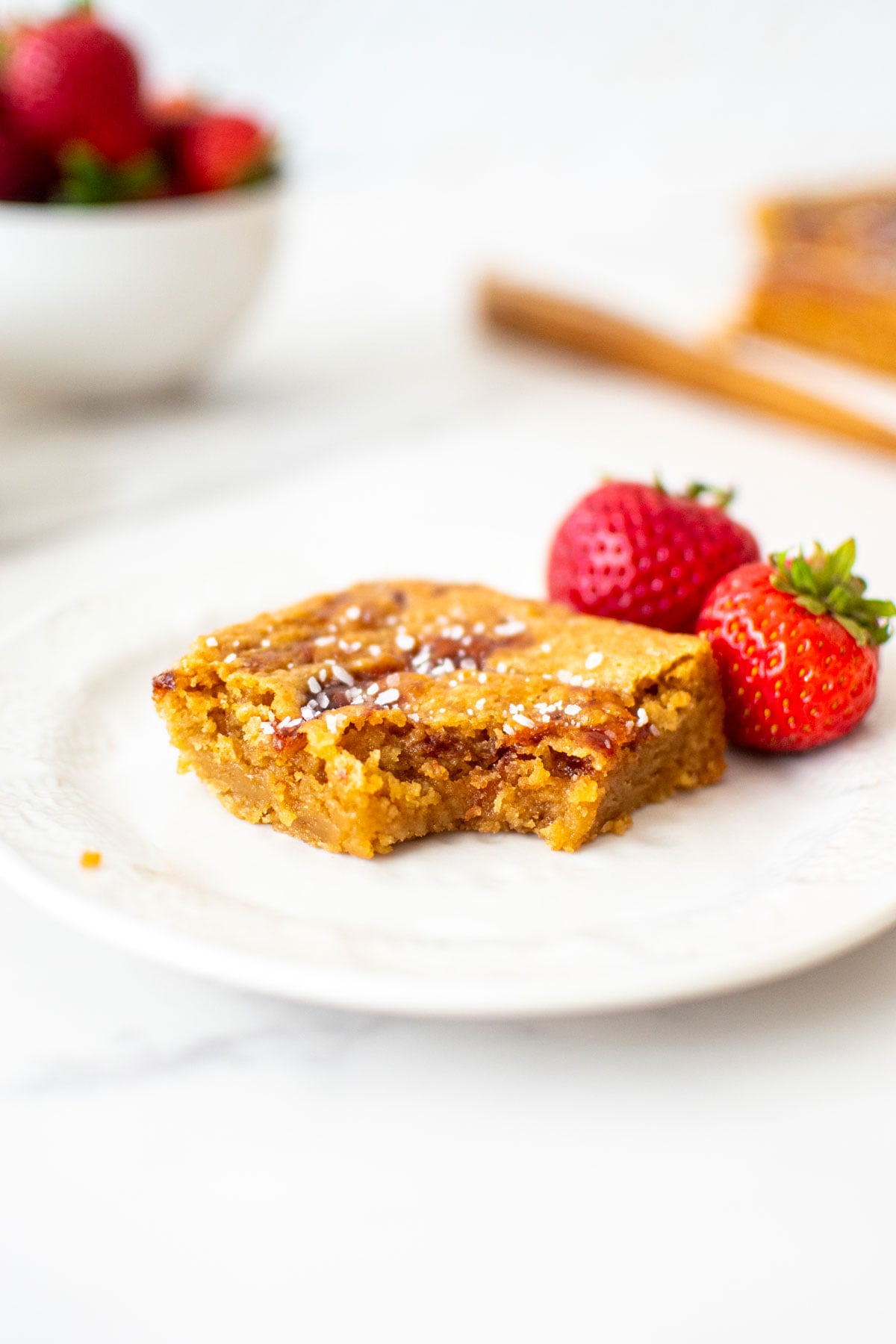olive oil strawberry blondie with a bite taken out on a white plate with fresh strawberries.
