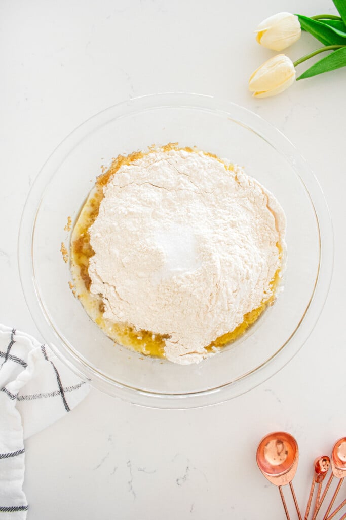 glass mixing bowl with wet and dry ingredients for blondies in it on a white marble counter.