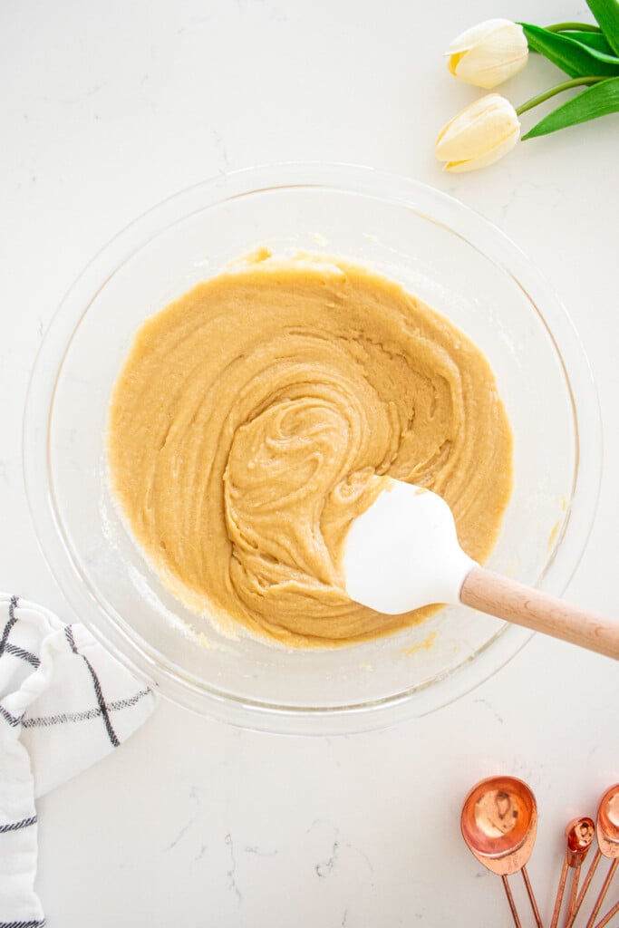 olive oil blondie batter mixed together in a glass mixing bowl with a spatula on a marble counter.