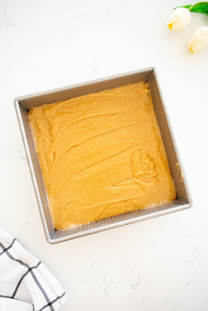 square baking pan with olive oil blondie batter spread evenly on a marble counter.