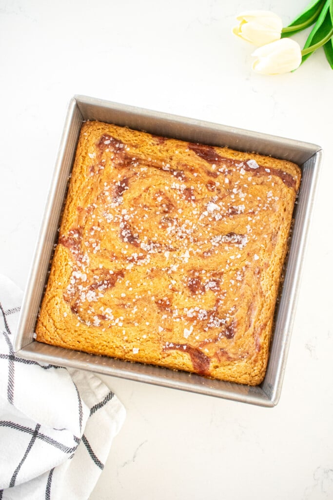 baked olive oil strawberry blondies with strawberry jam swirl and flaky sea salt on a marble counter.