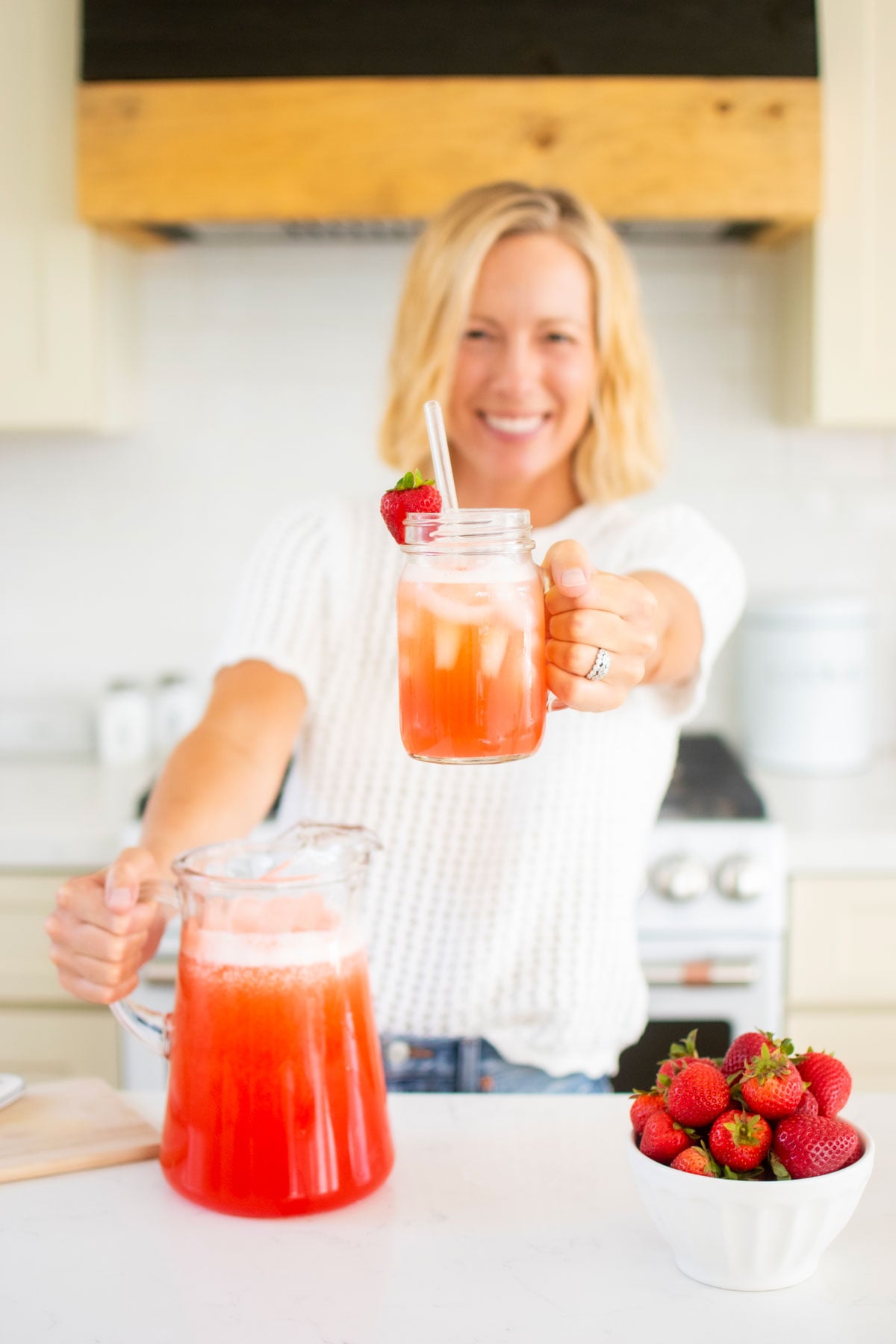 woman holding a mason jar glass of strawberry limeade at kitchen counter.