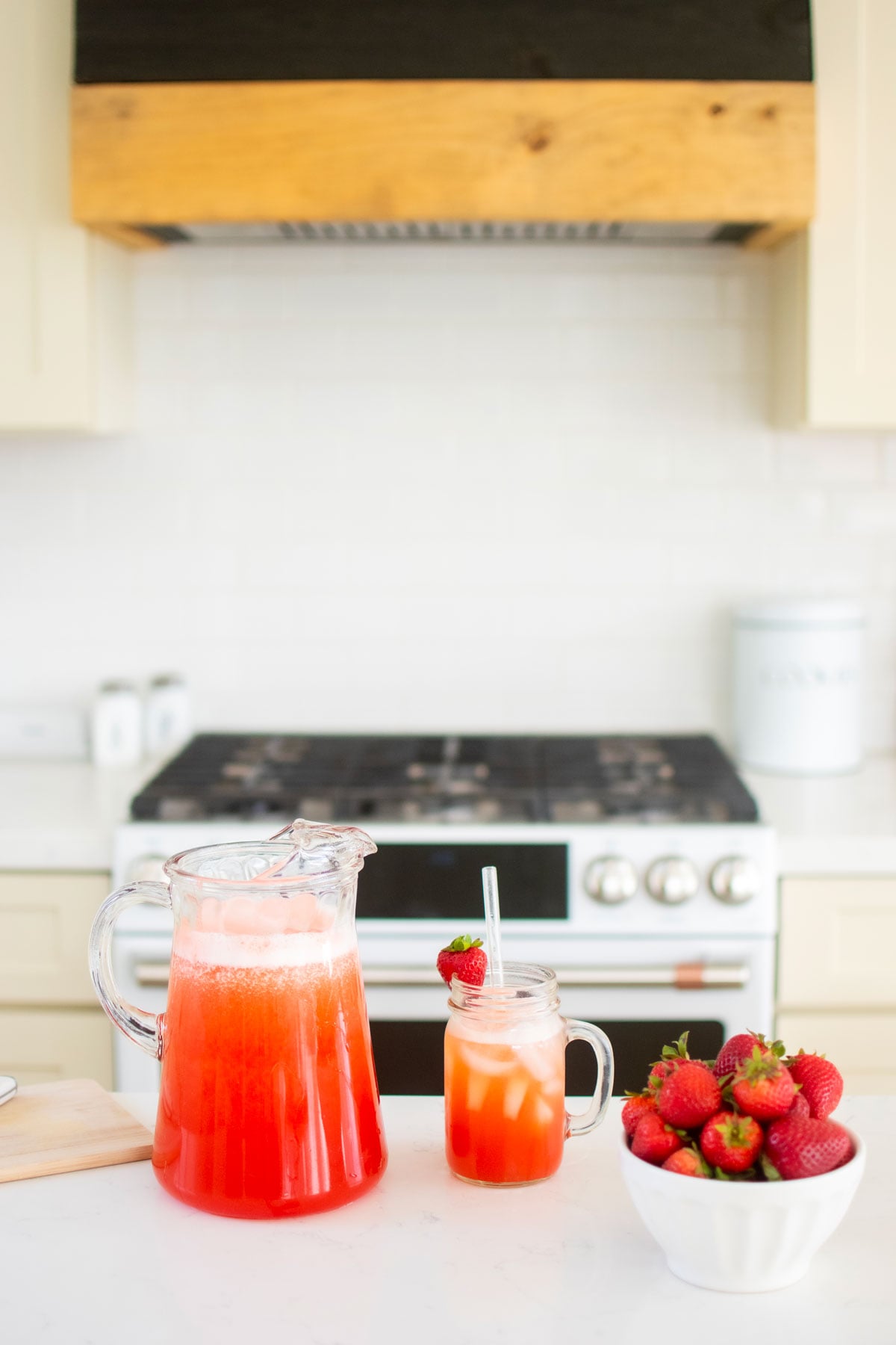 pitcher of strawberry limeade on a kitchen counter with a glass and fresh strawberries in a bowl.