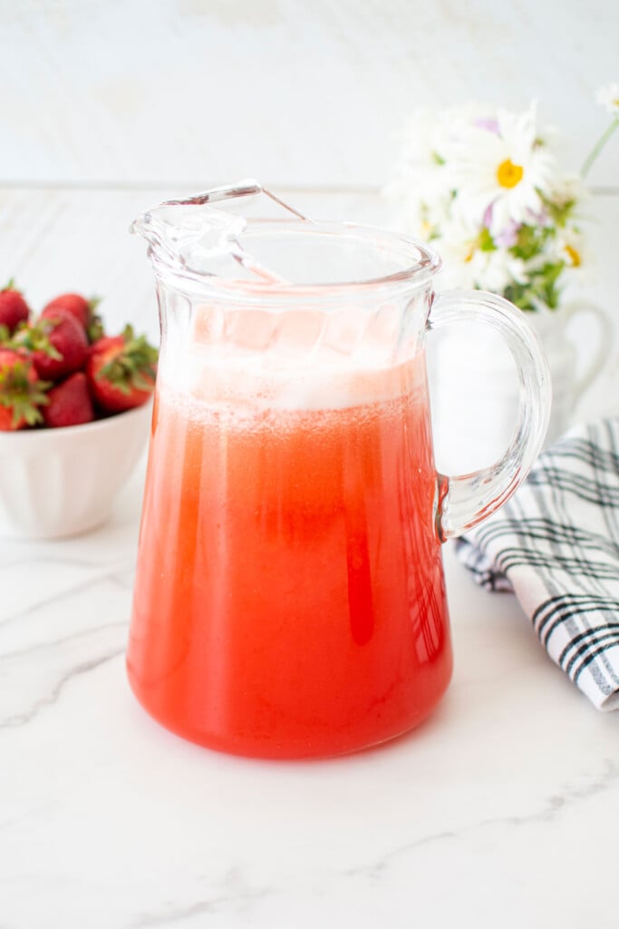 glass pitcher with strawberry limeade on a white marble countertop.