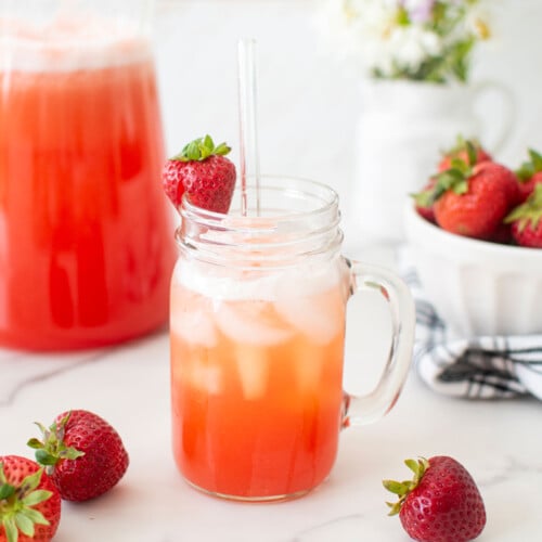 strawberry limeade in a mason jar glass with a fresh strawberry and a glass straw.