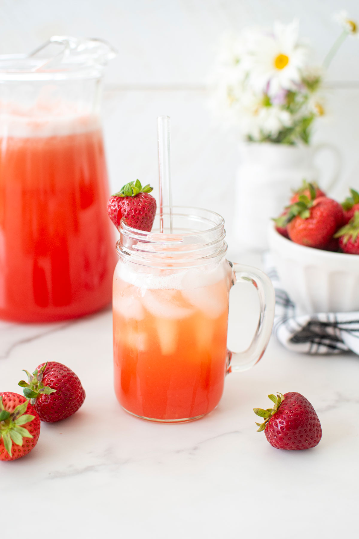 strawberry limeade in a mason jar glass with a fresh strawberry and a glass straw.