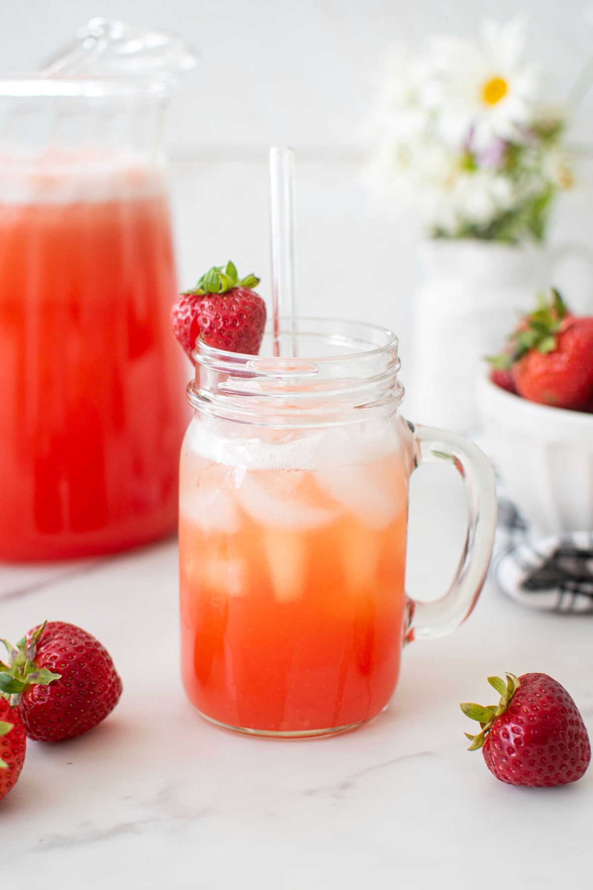 strawberry limeade in a mason jar glass with a fresh strawberry and a glass straw.