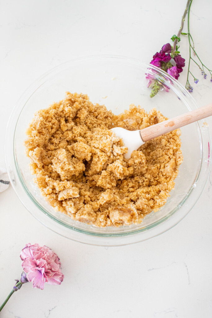 cherry pie bar dough in a glass mixing bowl with a spatula on a white marble counter with fresh flowers.